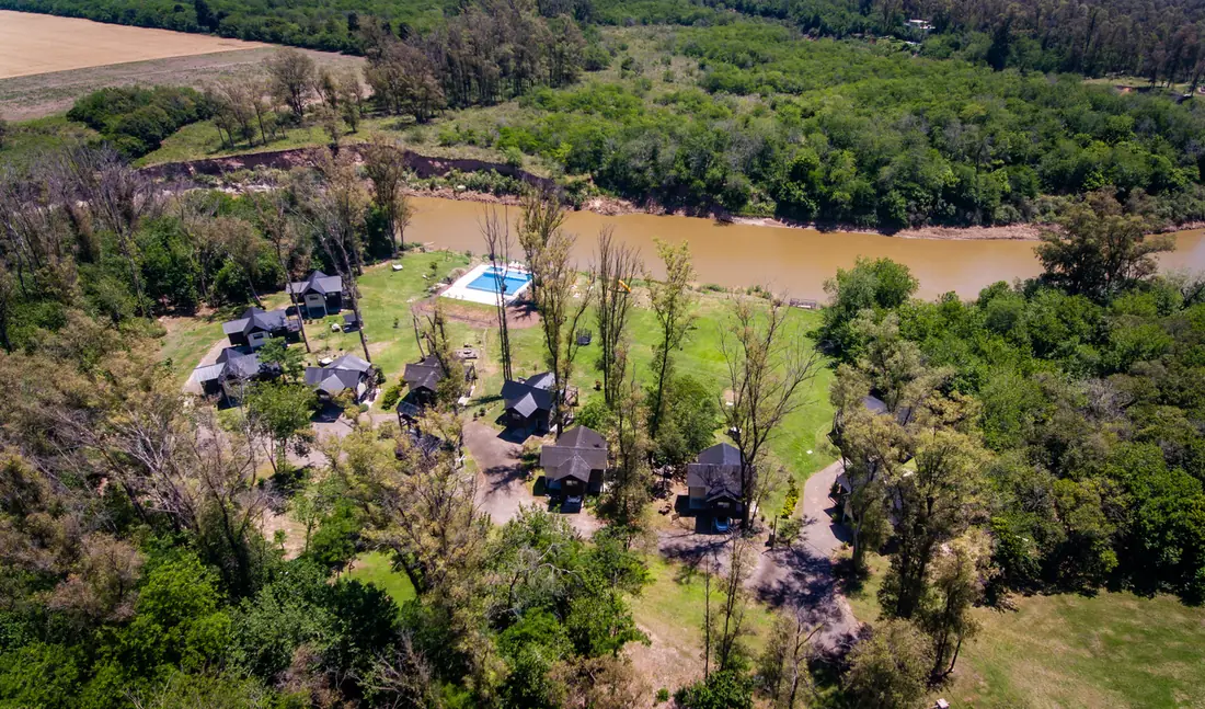 Vista aérea del complejo Alma de Río: cabañas, pileta y el río entre los árboles.