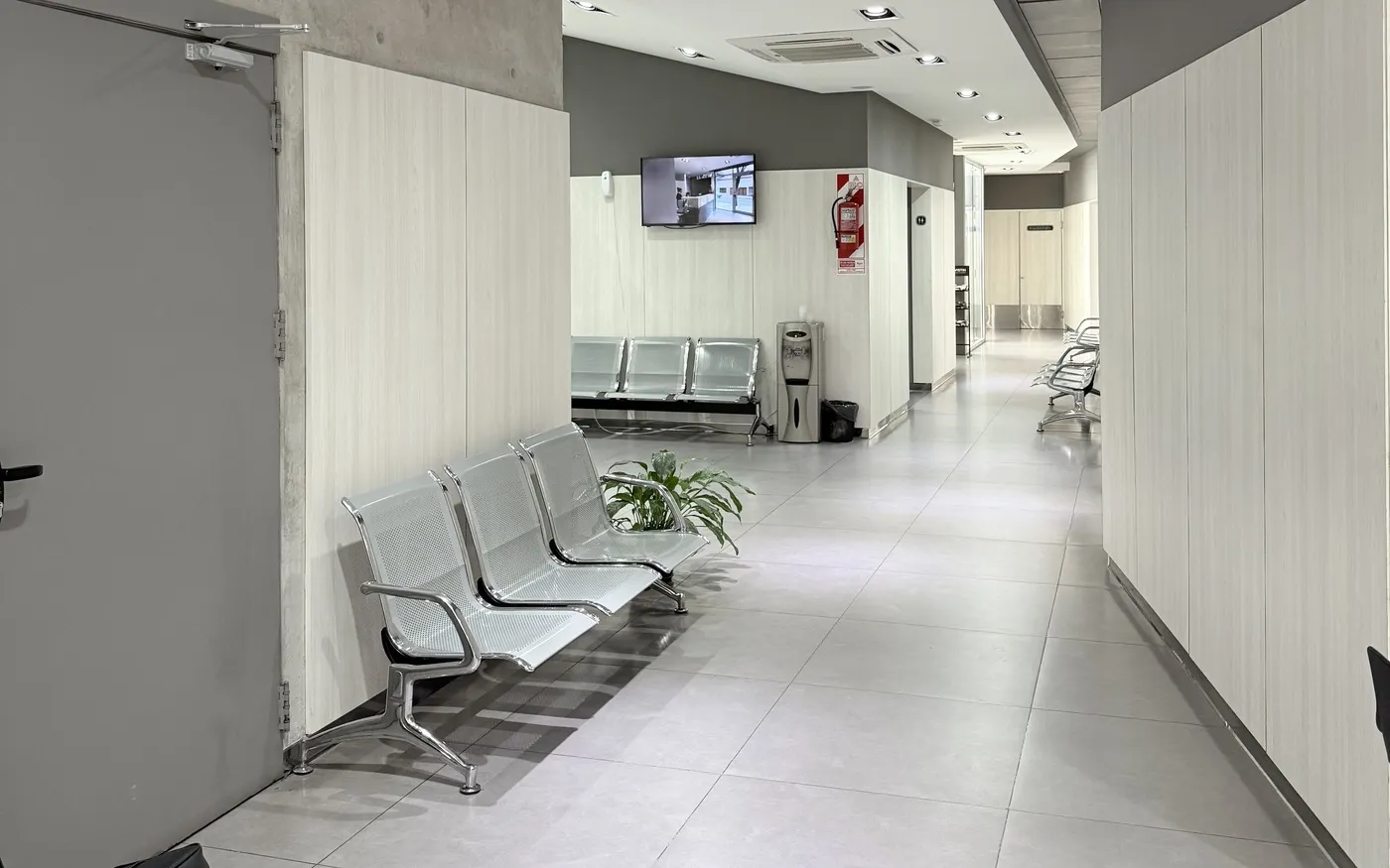 Sala de espera de una sede de COAS: pasillo con asientos y un televisor.